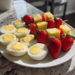 Plate with halved boiled eggs and fruit skewers of strawberries and pineapple for Easter party snack ideas