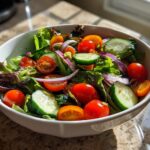 Bowl of fresh garden salad with cherry tomatoes, cucumber slices, red onion, and leafy greens.