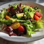 Fresh spring salad with avocado, cherry tomatoes, and mixed greens on a white plate.