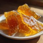 Close-up of golden brittle candy pieces on a white plate, showcasing homemade candy recipes.