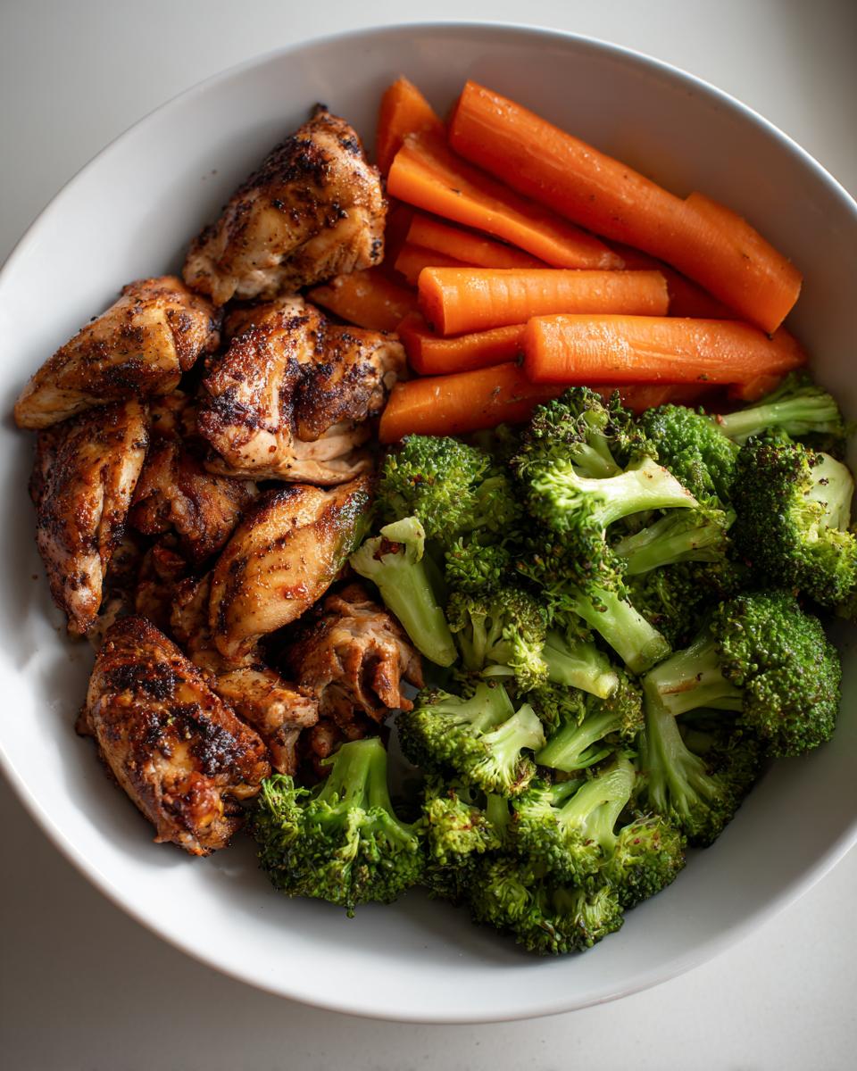 Grilled chicken pieces with steamed broccoli and carrots in a white bowl for high protein dinner recipes.
