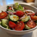 Bowl of healthy spring salads with cherry tomatoes, cucumber slices, red onion, and mixed greens.