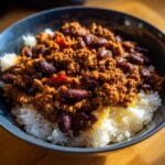 Bowl of chili with ground meat and kidney beans served over white rice, a budget friendly meals option.