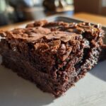 A close-up shot of a moist and fudgy homemade brownie slice on a white plate.