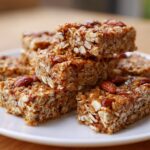 Close-up of homemade granola snacks stacked on a white plate with visible oats and almonds.