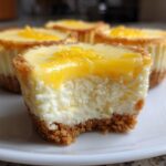 Mini lemon cheesecake bites with a graham cracker crust and lemon topping on a white plate.