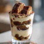 Mini tiramisu dessert cups layered with cream and cocoa powder in a clear glass.