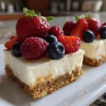 Two squares of no bake cheesecake topped with strawberries, raspberries, and blueberries.