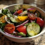 Bowl of quick salad side dishes with cherry tomatoes, cucumber slices, red onion, and greens.