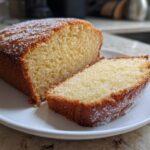 Close-up of a sugar-topped pound cake loaf with a sliced piece on a white plate for easy baking recipes