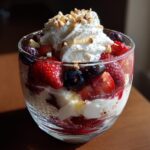 Glass cup filled with spring berry desserts topped with whipped cream and chopped nuts.