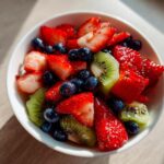 Bowl of spring fruit desserts featuring sliced strawberries, kiwi, and blueberries.