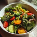 Bowl of fresh spring potluck side dishes with mixed greens, cherry tomatoes, and cucumber slices