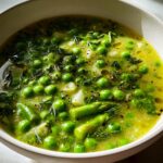 Bowl of spring soup recipes featuring green peas, asparagus, herbs, and broth.