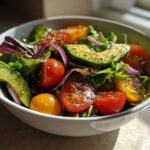 Bowl of fresh spring vegetarian dinners salad with avocado, cherry tomatoes, red onion, and mixed greens