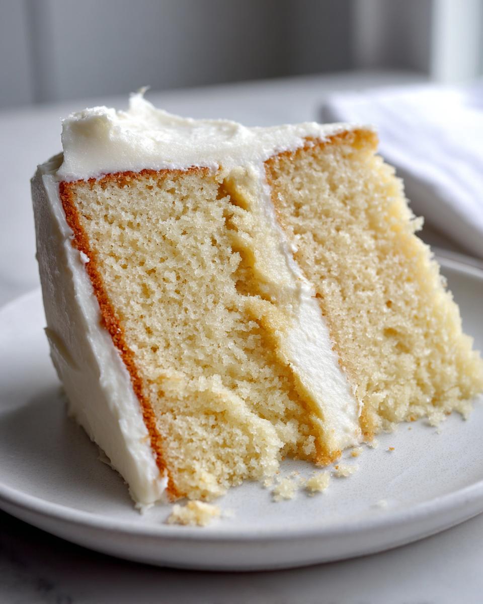 Close-up of a slice of vanilla cake with white frosting on a plate, perfect April holiday desserts