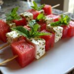 Watermelon feta skewers snack with fresh mint leaves on a white plate.