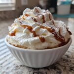 White bowl filled with whipped cream sweet dip topped with caramel drizzle and powdered sugar