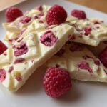 Close-up of white chocolate raspberry bark pieces garnished with fresh raspberries on a white plate.