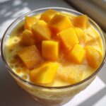 Glass bowl filled with creamy mango sago topped with fresh mango cubes.