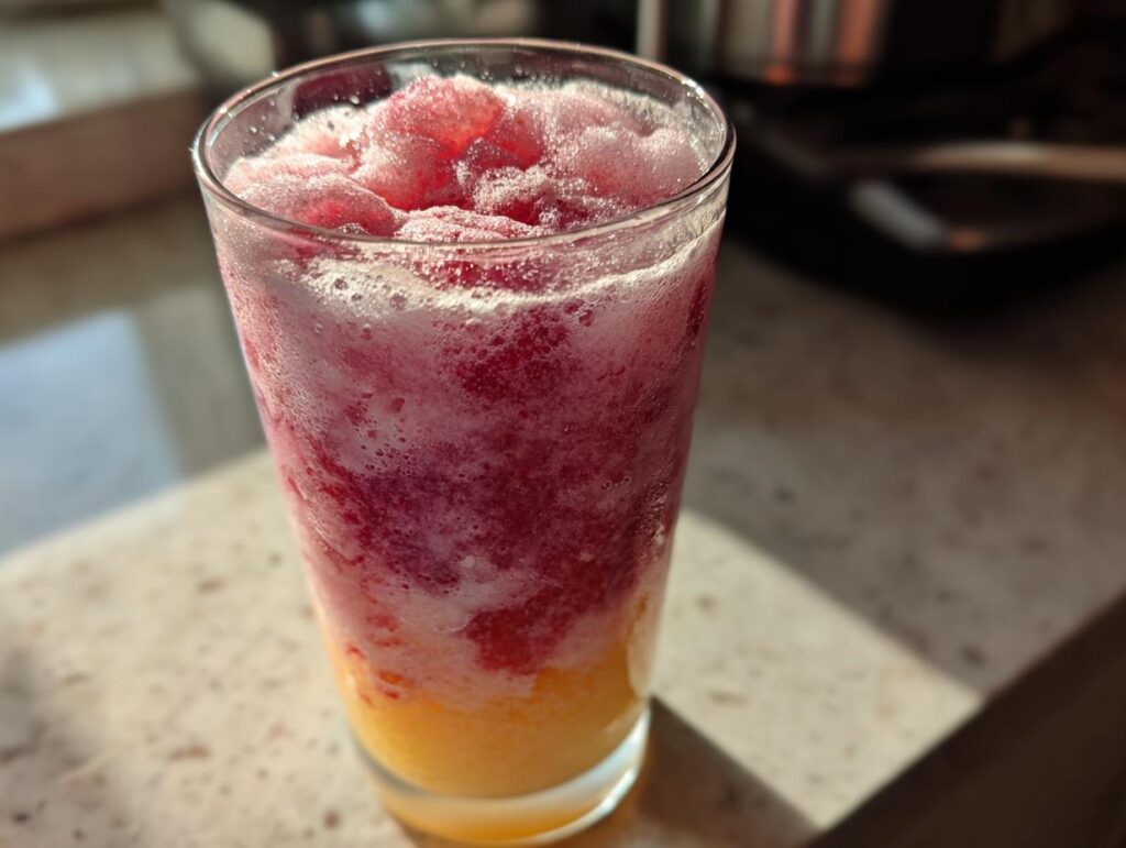 Glass filled with vibrant frozen strawberry lemonade showing red and yellow icy layers.
