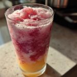 Glass filled with vibrant frozen strawberry lemonade showing red and yellow icy layers.