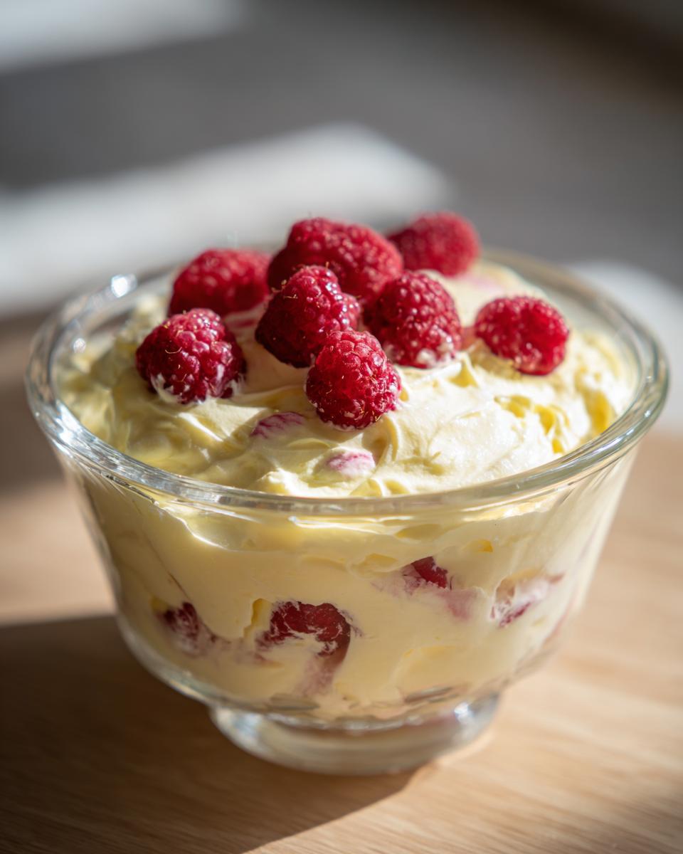 Glass bowl filled with creamy Lemon Raspberry Fluff topped with fresh raspberries.