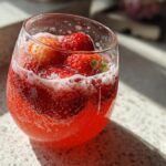 Glass of sparkling red summer mocktails with fresh strawberries and bubbles.